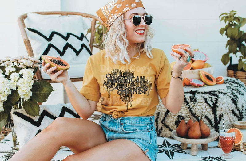 Blonde woman eating fruit while wearing an orange “American Honey” shirt.